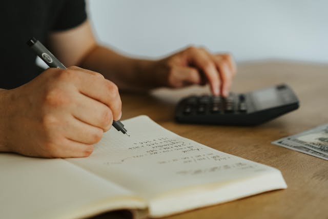 someone writing in a notebook with one hand and operating a calculator with the other
